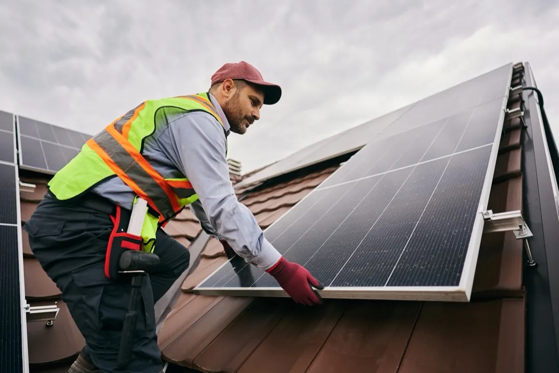 Monteur der Solarmacherei setzt ein Photovoltaik-Modul auf ein Ziegeldach